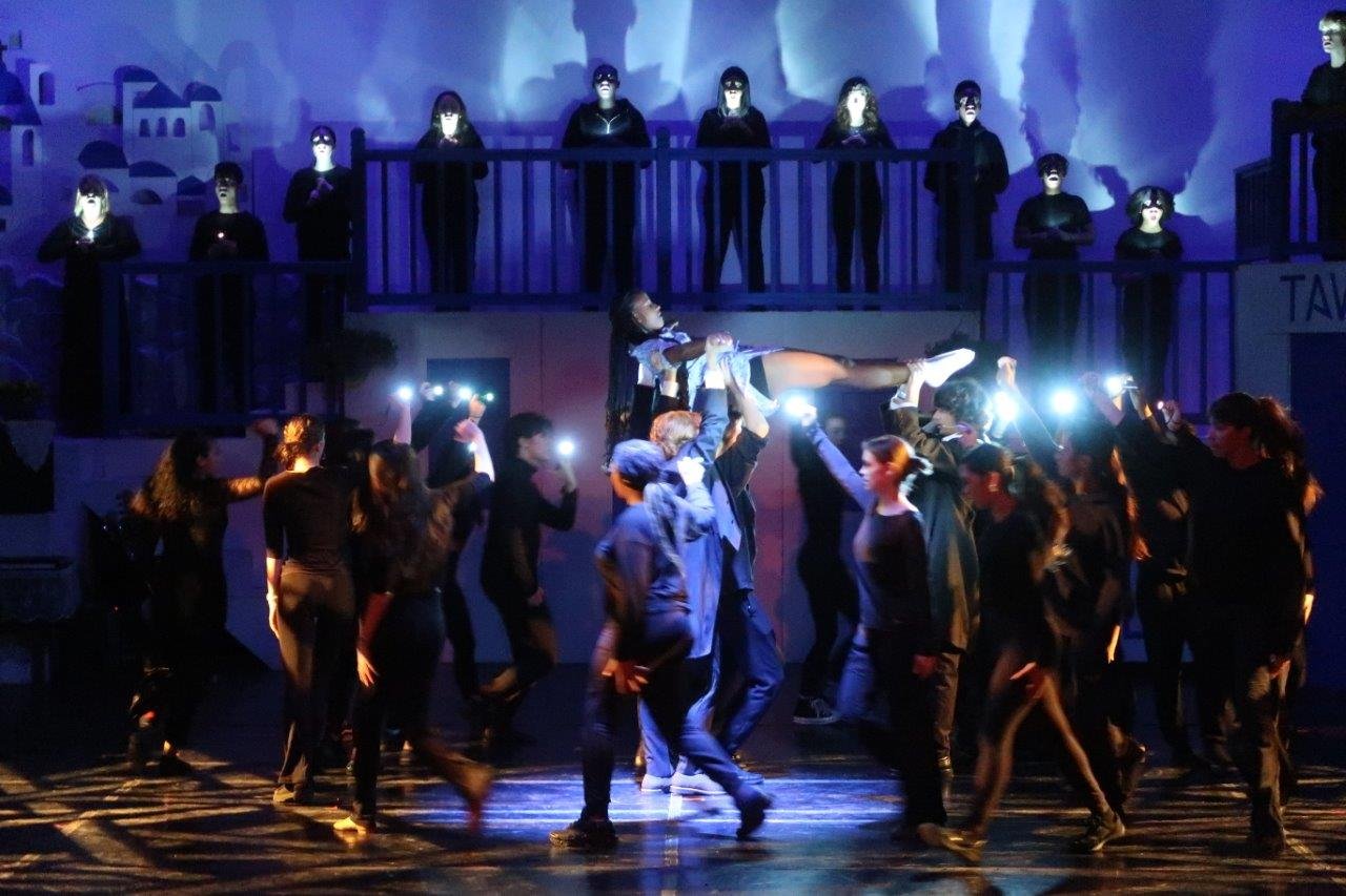  Sophie being carried in the air as dancers walk around her.  Background crew holding flashlights shining on Sophie. 