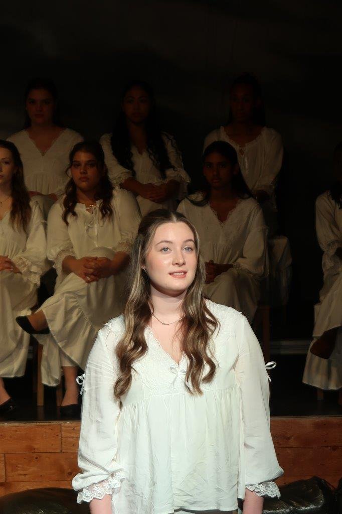  Actor dressed in white speaks as others look on from behind. 