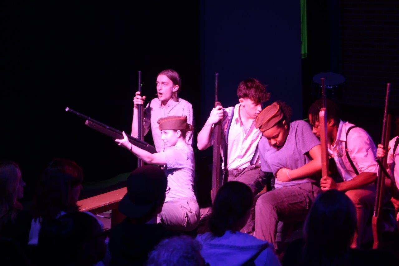  Actors carrying rifles crouched, with some preparing to aim their rifles to shoot. 