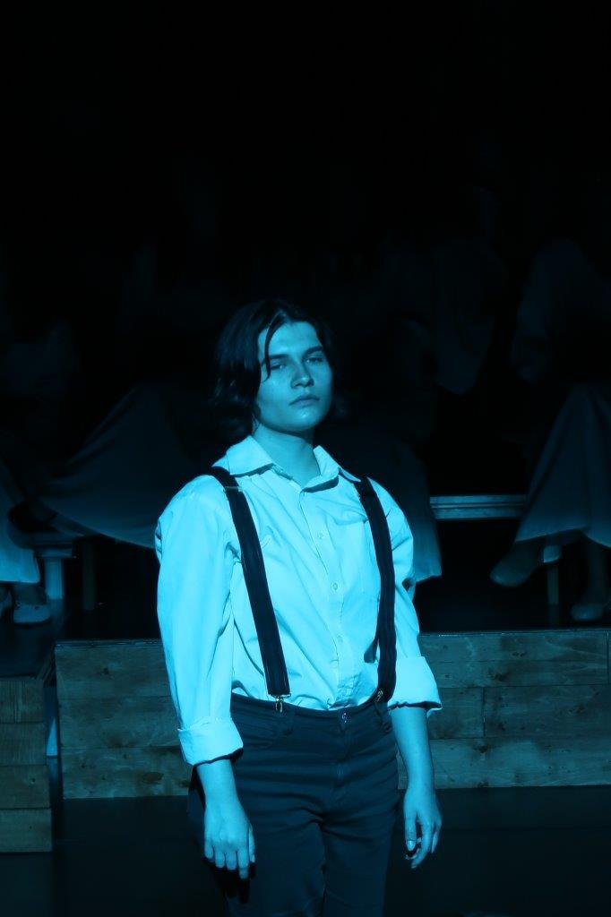  Actor in white shirt and suspenders looking forward in a grey light. 