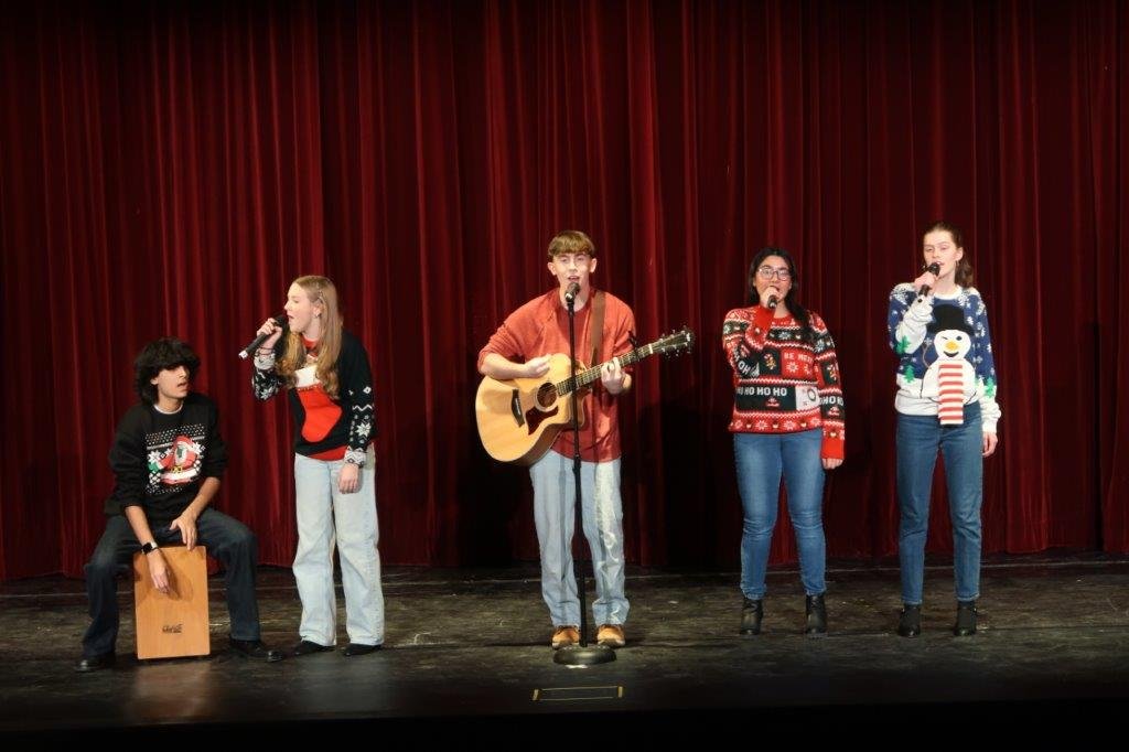  Group of 5 singers, with singer on far left sitting on a beatbox and middle singer playing a guitar. 