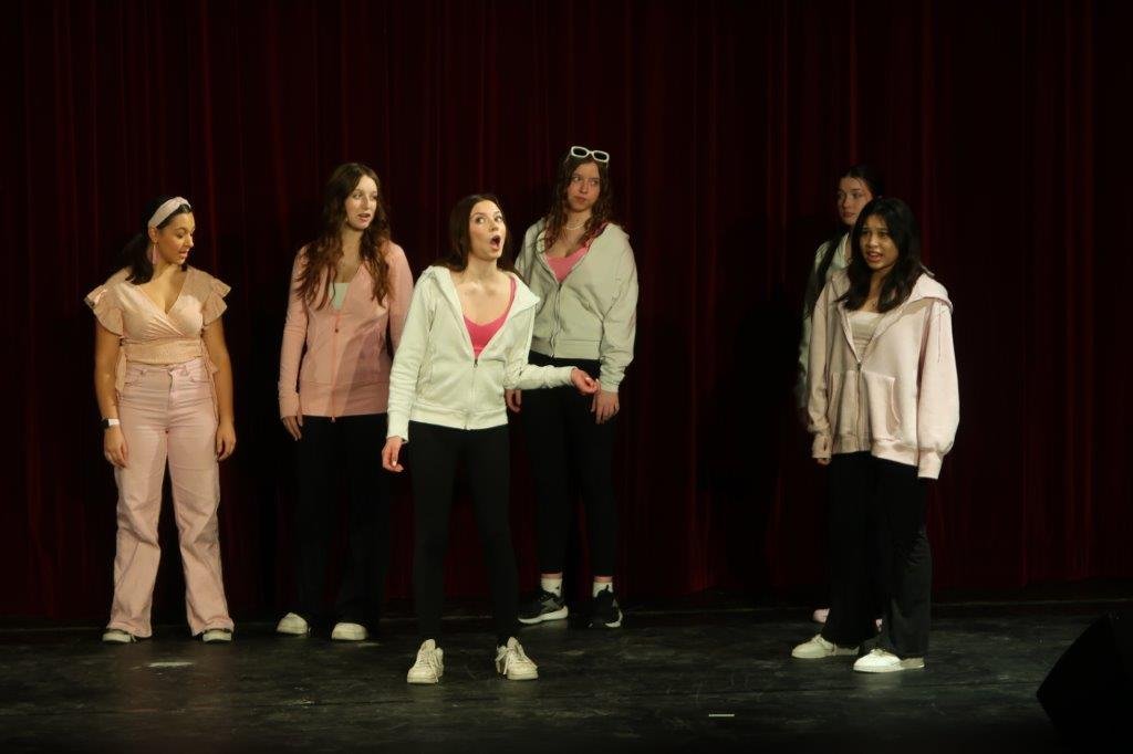  Actors dressed in shades of pink and white against a black backdrop. 