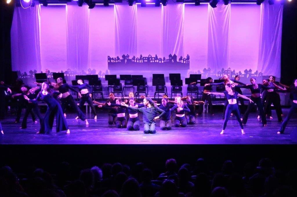  Three groups of dancers on stage; the ones on the left and right are standing while the middle group is kneeling. 