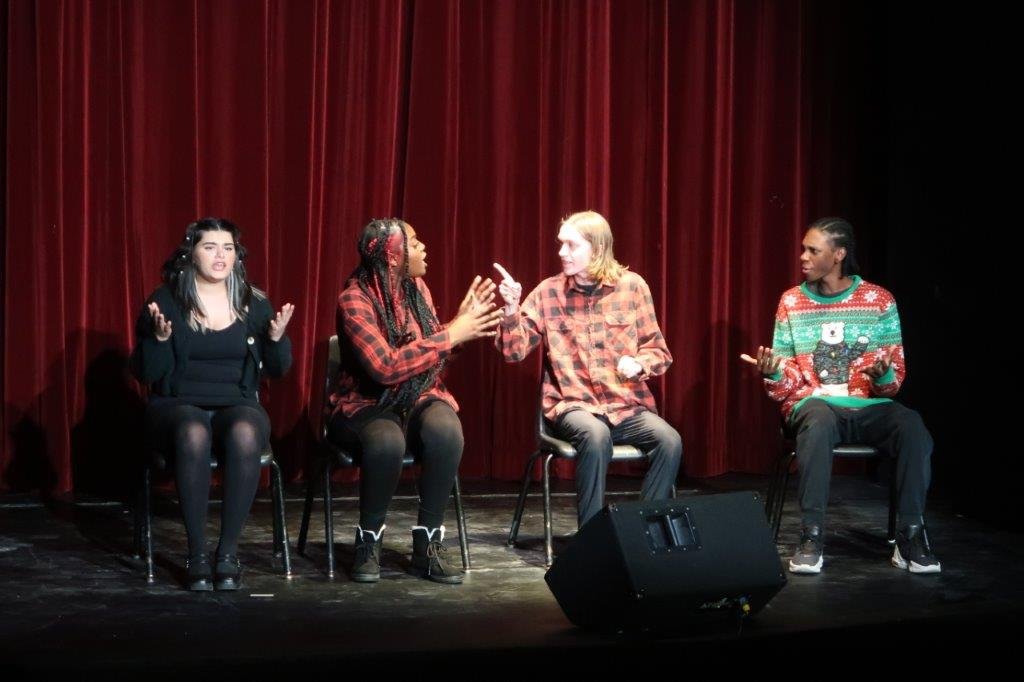  Four actors appearing to be arguing whilst seated. 