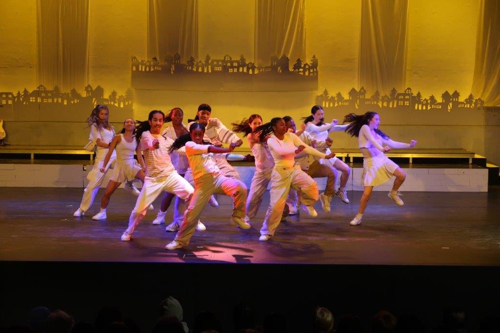  Dancers dressed in white dancing with their left legs lifted up. 