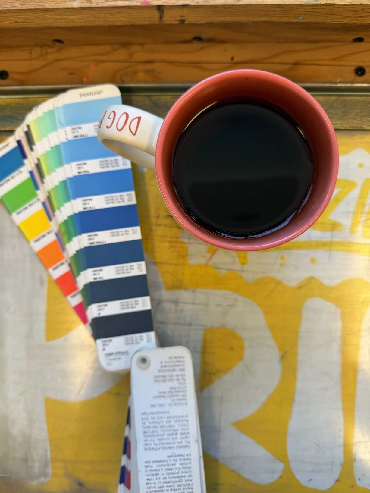 Pantone ink mixing chart and a cup of coffee on a letterpress inking table.