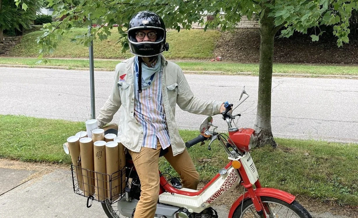 Letterpress Poster Printer Alexander Landerman on his 70's area moped with a basket full of prints to deliver