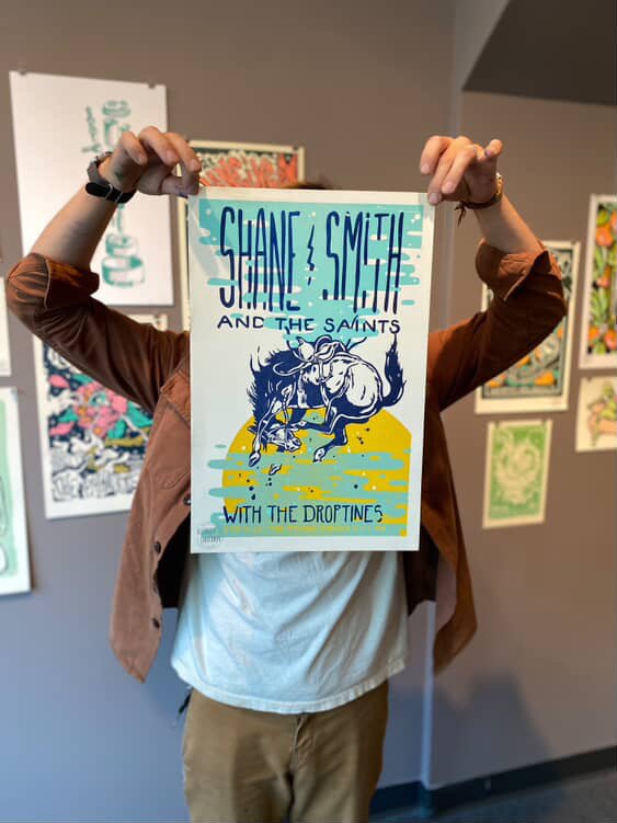 Letterpress printer holding a hand-printed show poster for Shane Smith and the Saints