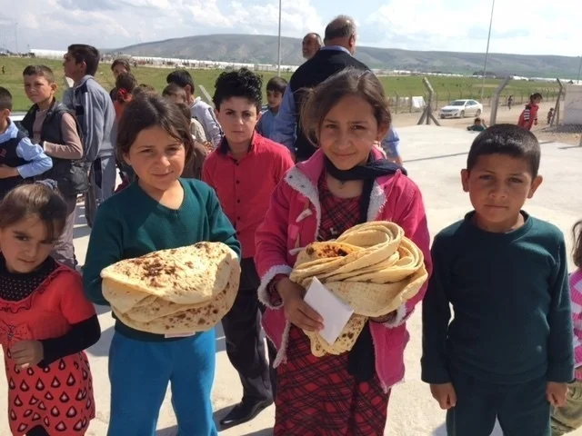 Yazidi IDP children in Iraq, holding bread they were rationed from a new bread bakery, built in the camp to provide food.