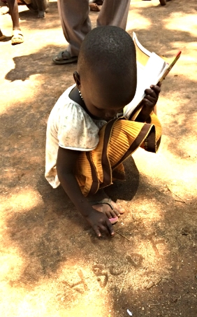Three year-old girl writing her ABCs in the dirt.