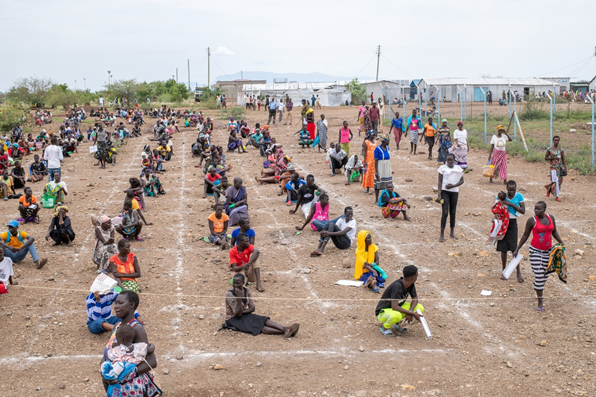 South Sudanese refugees practice physical distancing against COVID as they await the distribution of  food rations.