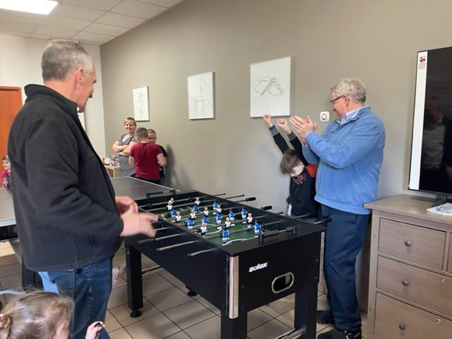   Mark Mueller, Tom Boone, Emma and Artem playing table soccer purchased with gifts from The Outreach Foundation.  