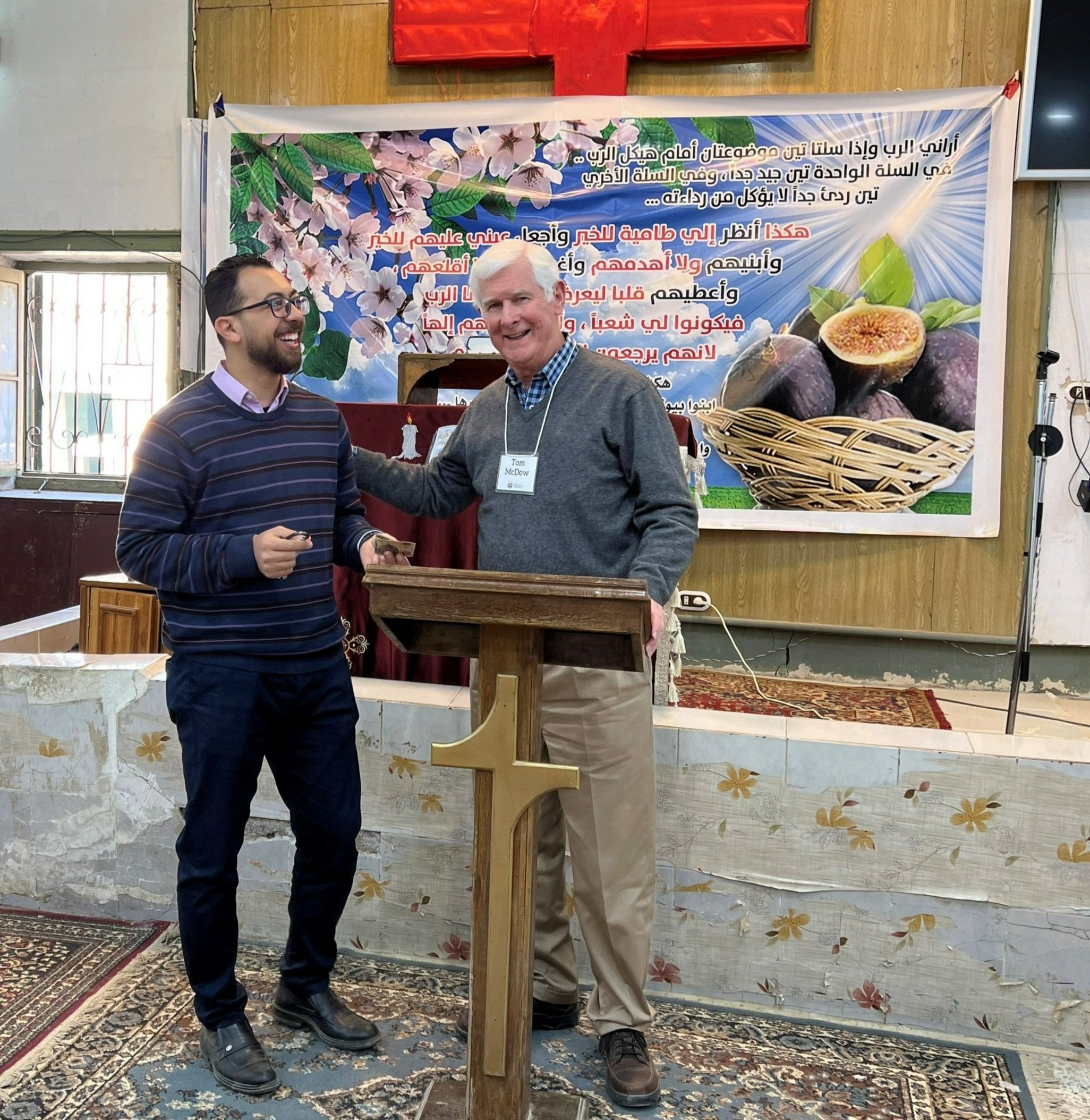  Tom McDow presented crosses shaped from the red Alabama mud where Tom grew up to pastors we visited; here he gives one to seminarian Amir, who, with his wife Irini, is doing fruitful ministry at Tamiya church and other areas in Fayoum. The banner be