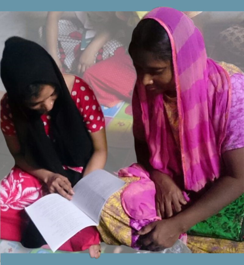 Two women wearing headscarves are sitting on a floor leaning over a book. They are reading.