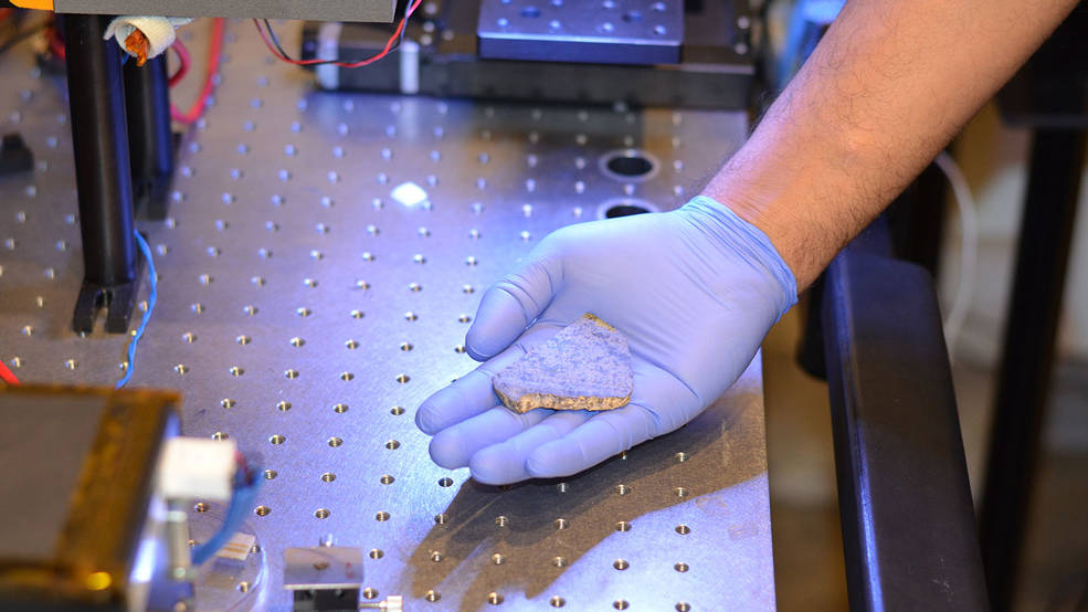 Rohit Bhartia of NASA's Mars 2020 mission holds a slice of a meteorite scientists have determined came from Mars. One of two slices will be used for testing a laser instrument for NASA's Mars 2020 rover while it's still on Earth; the other slice will go to Mars onboard the rover. Credits: NASA/JPL-Caltech