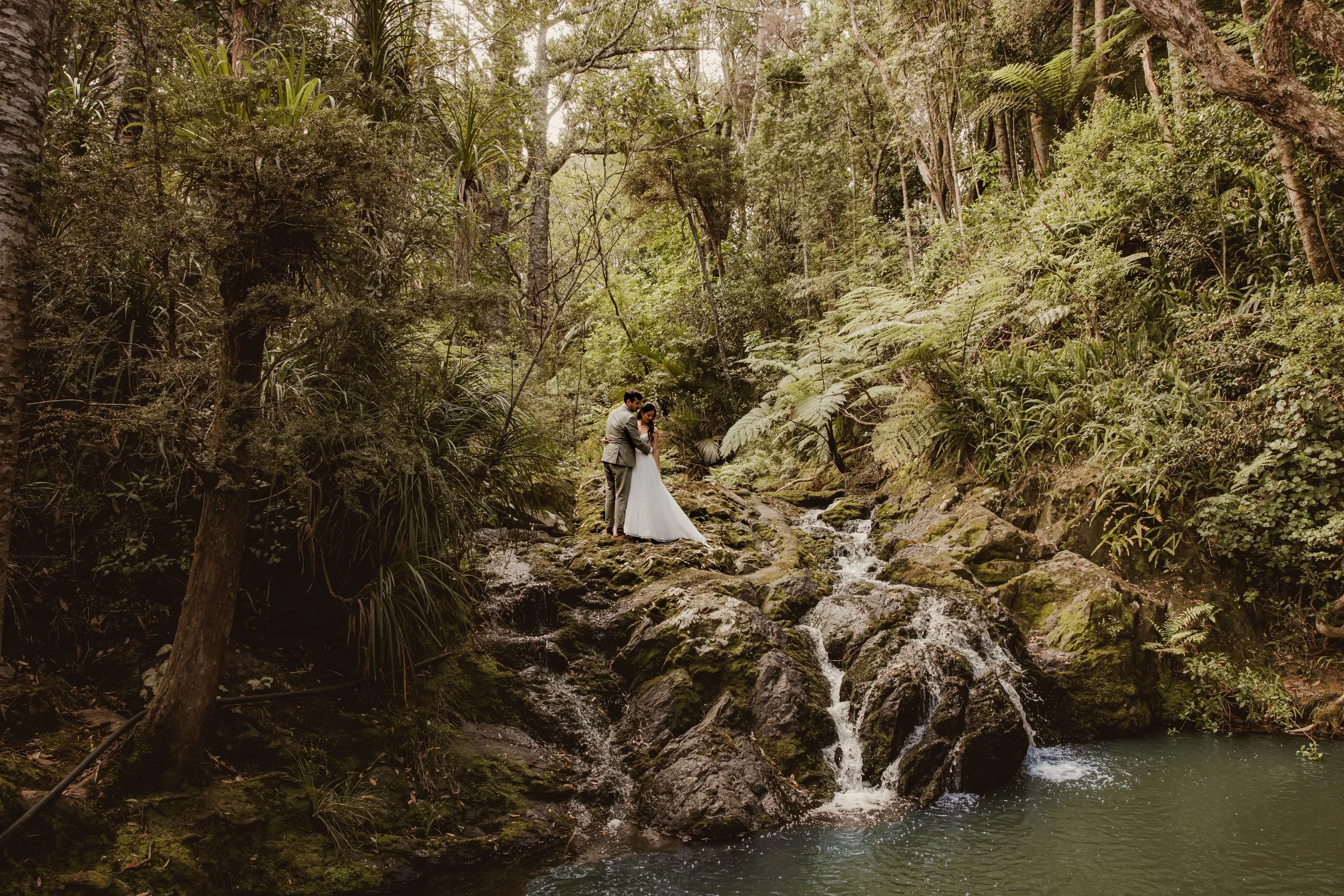 Bride and groom kissing on a beach boardwalk, with sand dunes and ocean in the background.