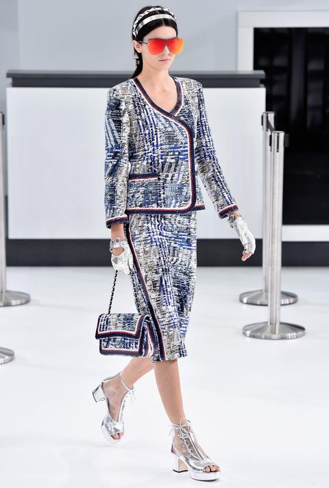 Another day, another runway win for Kendall Jenner . Or, make that a double win. The reality star slash model starred in Karl Lagerfeld's latest production, in which he transformed the Grand Palais into a Chanel-branded airport terminal, complete with check-in counters, a baggage drop-off, and stewardesses. And as a stylish jet-setting pro IRL , Jenner played her role in the Chanel spring 2016 show to perfection. First she breezed through the concourse in a trimmed tweed ladylike skirt set—modernized with an onslaught of futuristic accessories, including silver headbands, cool orange shades, metallic silver moto gloves, and see-through lace-up platform booties ( above ).