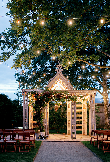 Red flowers and greenery climb up this white wooden arbor for a romantic, vintage look. Photo: Emily Wren Photography
