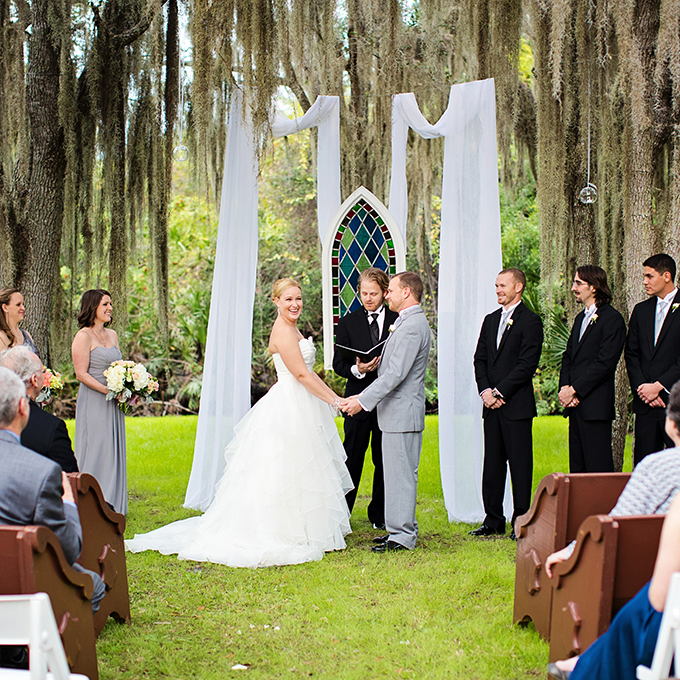 A classic-meets-modern wedding altar consisting of draped fabric and a floating stained glass window. Photo: Angel Gray Photography