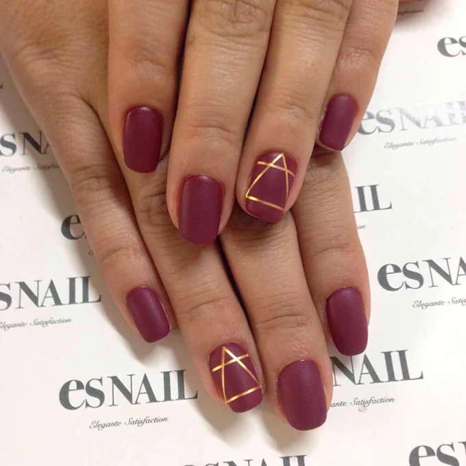 A scarlet manicure with a geometric gold detail. Photo: es Nail via Instagram