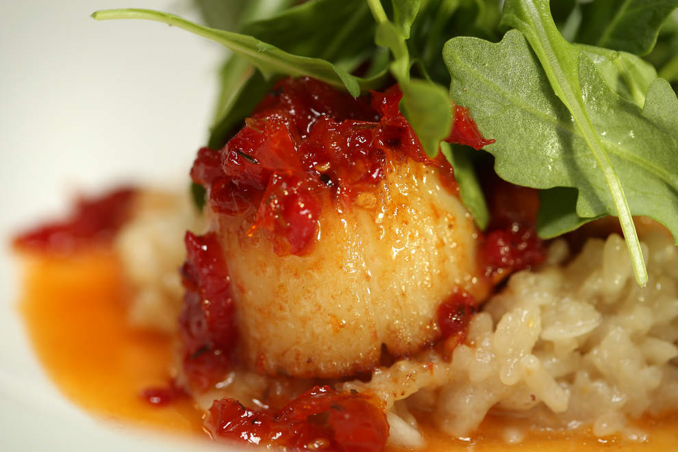 Pan-Seared Sea Scallops at Ambrosia in Eugene is plated on a bed of risotto and topped with sun-dried tomato honey glaze along with arugula. (Collin Andrew/The Register-Guard)