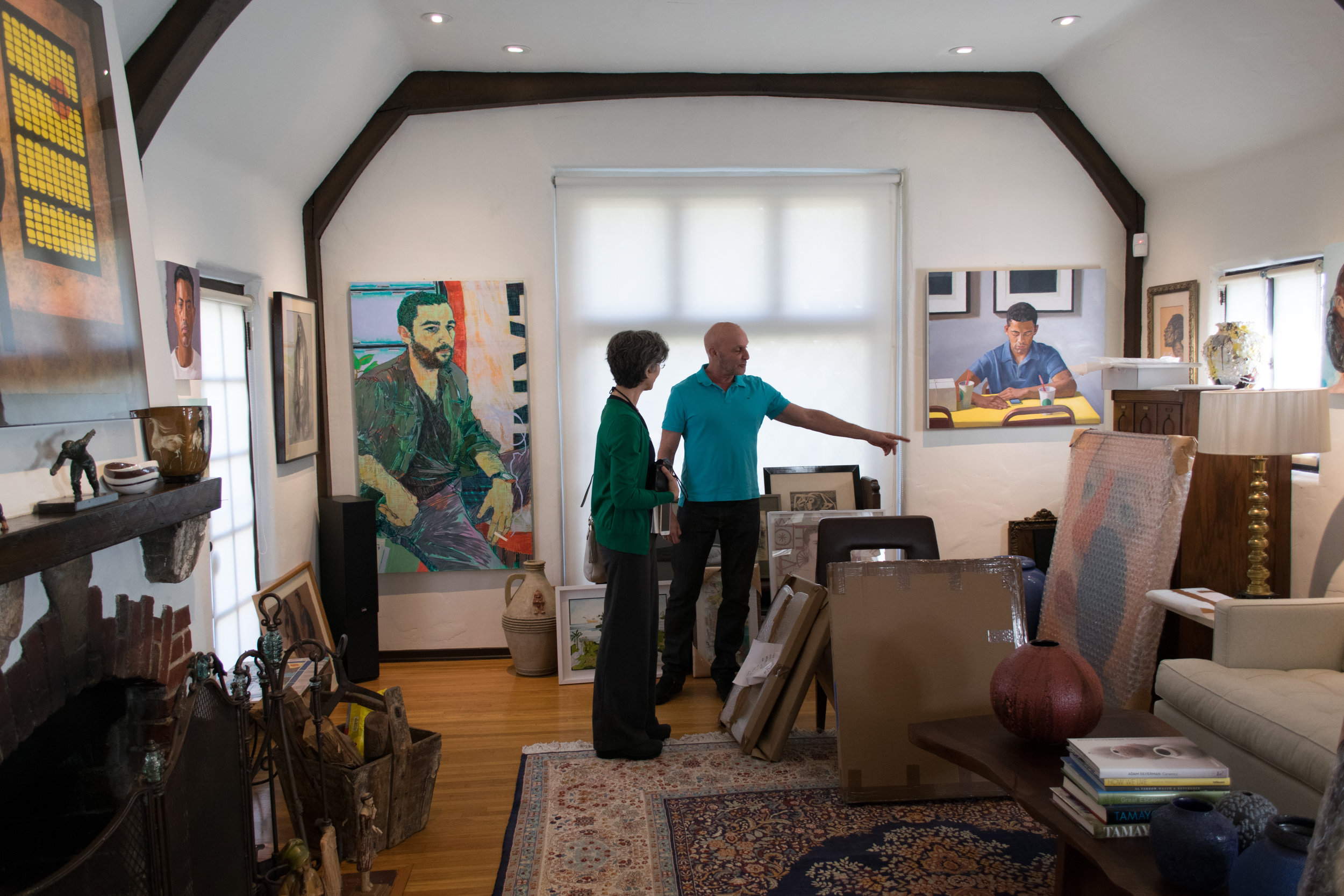Daena Title standing next to Robert as he points to new work he has not yet unpacked.Behind on the walls are works by, at left, Hope Gangloff, and at right, Dan McCleary.