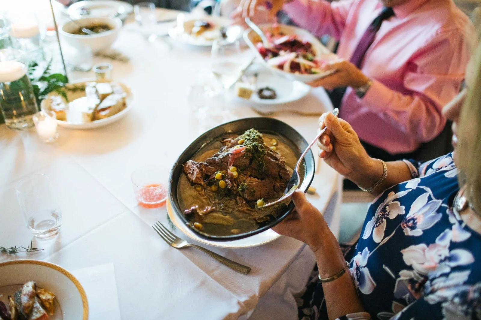 An elegant family-style wedding dinner featuring a beautifully roasted dish being delicately served by a guest at the table.