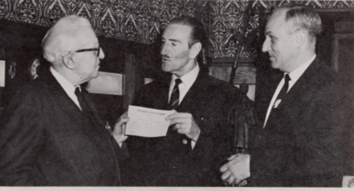 Vincent Starrett awards Basil Rathbone with membership in the Hounds of the Baskerville (sic). Robert Hahn, who was head of Hugo’s Companions, also of Chicago, also awarded Rathbone membership in the group. Rathbone was in Chicago in the mid-60s to film introductions to television station WGN’s series, “The Sherlock Holmes Theater.” Photo from the HK Kronicle, the house organ for the employees of H. Kohnstamm and Co., where Hahn was credit manager for the Chicago office.