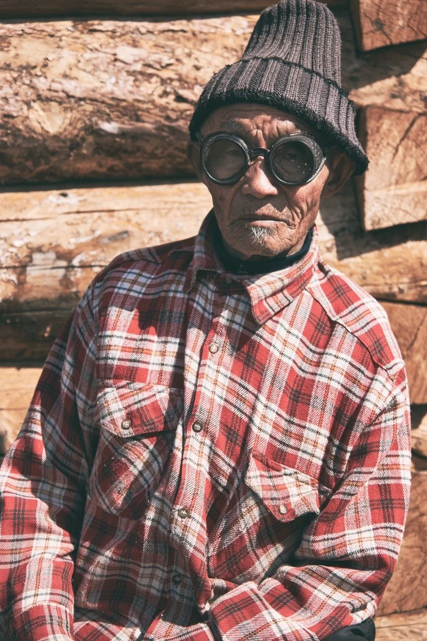 Elderly man wearing a plaid shirt and beanie with large round glasses. Film Mongolia. Filming in Mongolia. Producer in Mongolia. Film Production Service in Mongolia. Fixer Service Mongolia.