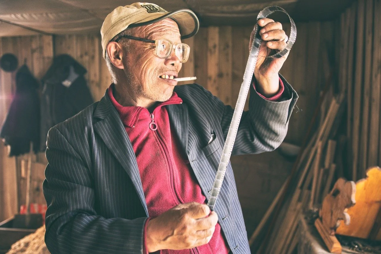 Man in glasses and cap holding film reel in a wooden room. Film Mongolia. Filming in Mongolia. Producer in Mongolia. Film Production Service in Mongolia. Fixer Service Mongolia.
