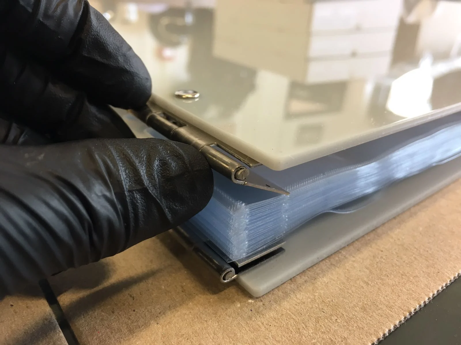 Hand showing the corner of a grey acrylic perspex portfolio album and how the sleeves are bound within binding-posts and stainless steel hinges