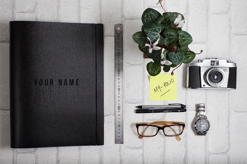 Name personalised bespoke portfolio in black A4 leather pictured with a vintage camera and other artists tools