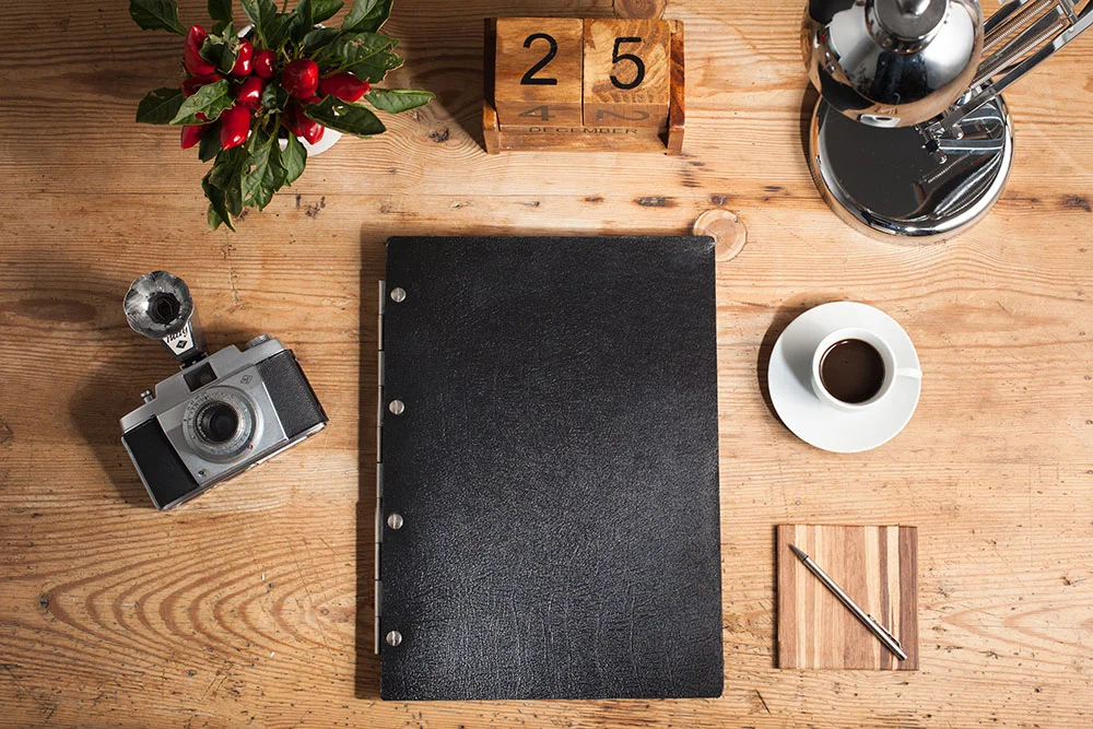 A4 portrait leather portfolio on a desk next to an espresso, camera, plant and chilli plant