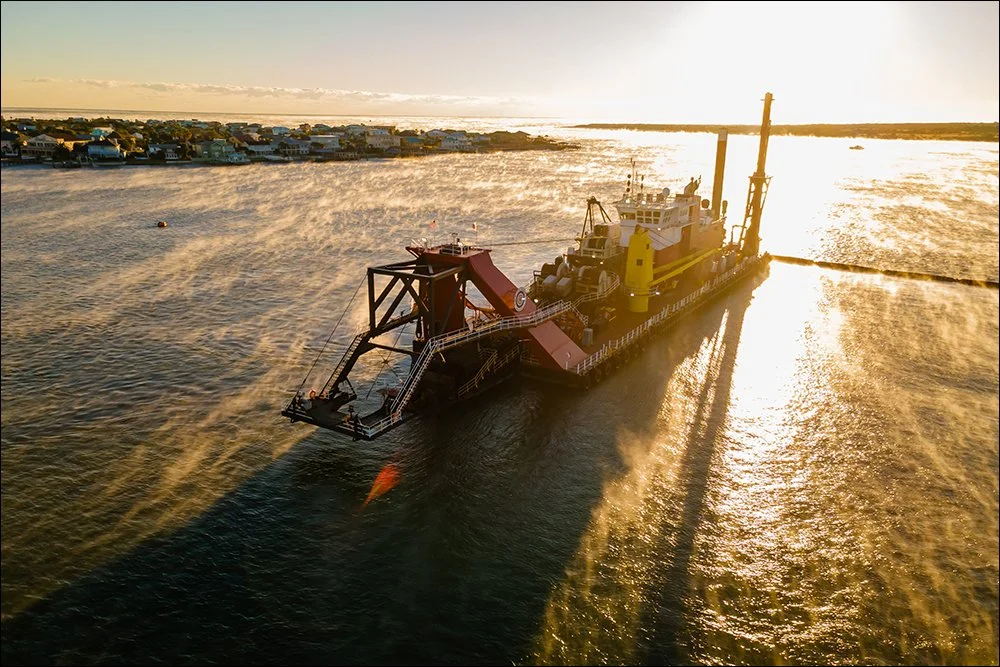 Aerial view of dredging equipment operating in coastal waterway at sunset