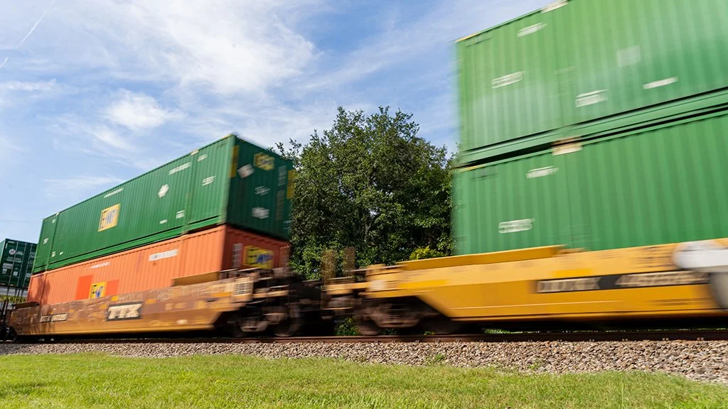 Freight train carrying stacked shipping containers moving at speed along the Florida East Coast Railway line