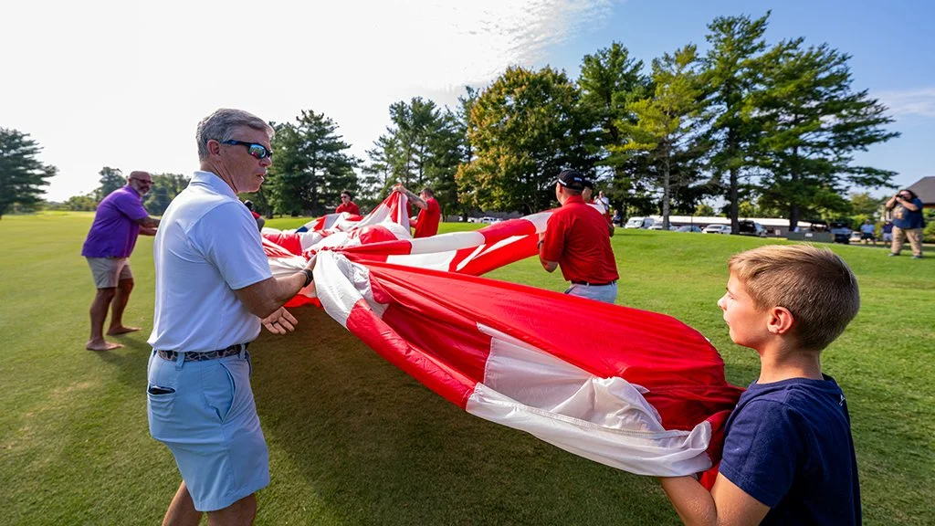 General Bryan Fenton, Miki Padgett, his son and volunteers gather the 50-foot American flag after the Team Fastrax parachute jump at Pars With Patriots.