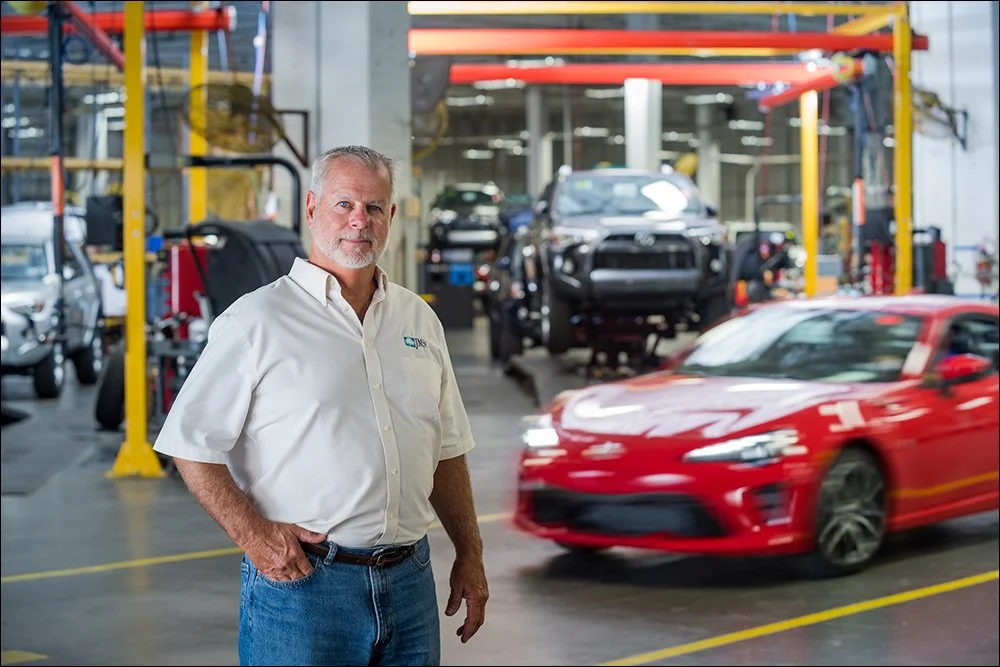Employee portrait in automotive service facility with vehicles and equipment in background