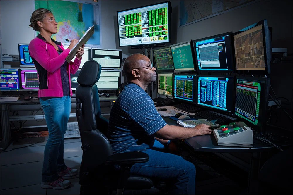 Technicians monitoring systems in industrial control room with multiple data screens