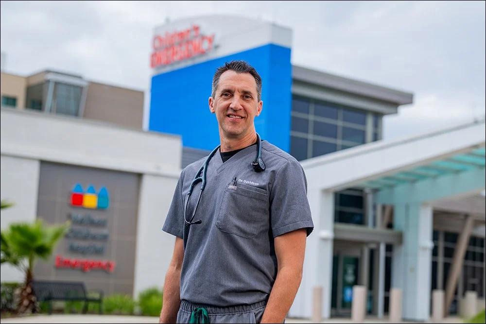 Physician portrait outside hospital entrance wearing scrubs and stethoscope
