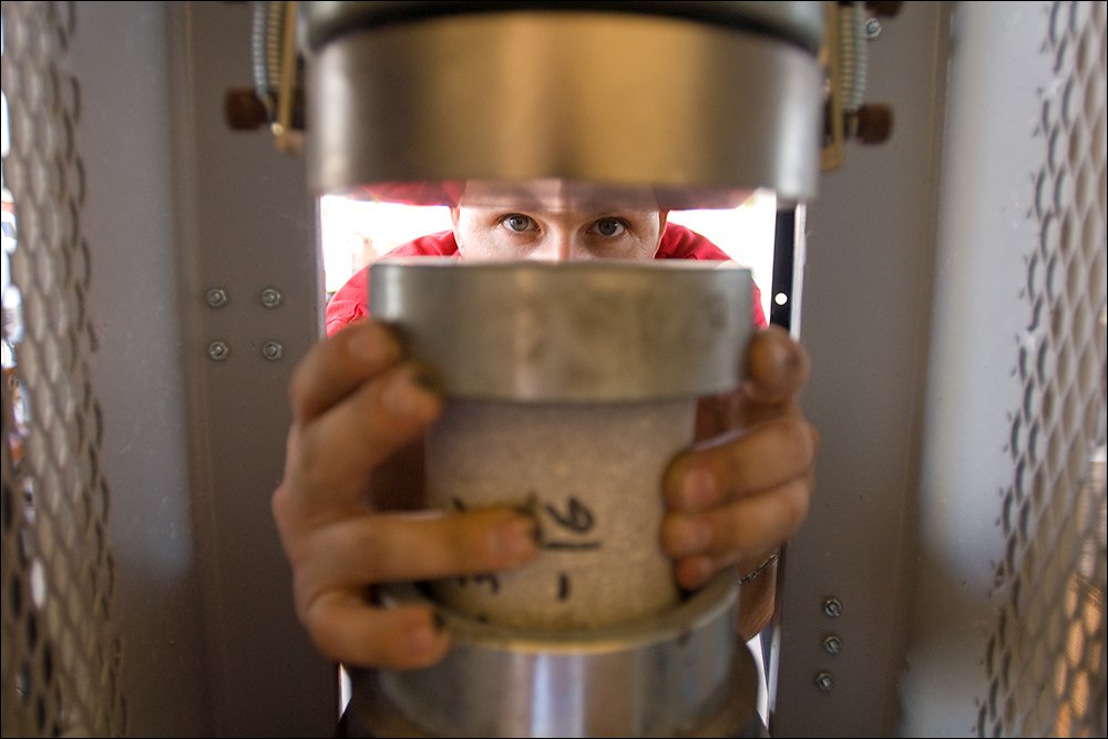 Technician placing material sample into compression testing machine in industrial lab