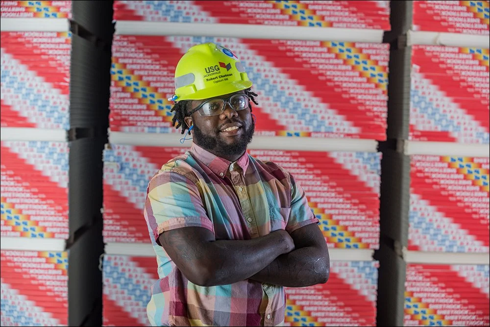 Manufacturing employee portrait standing in front of stacked building materials in facility