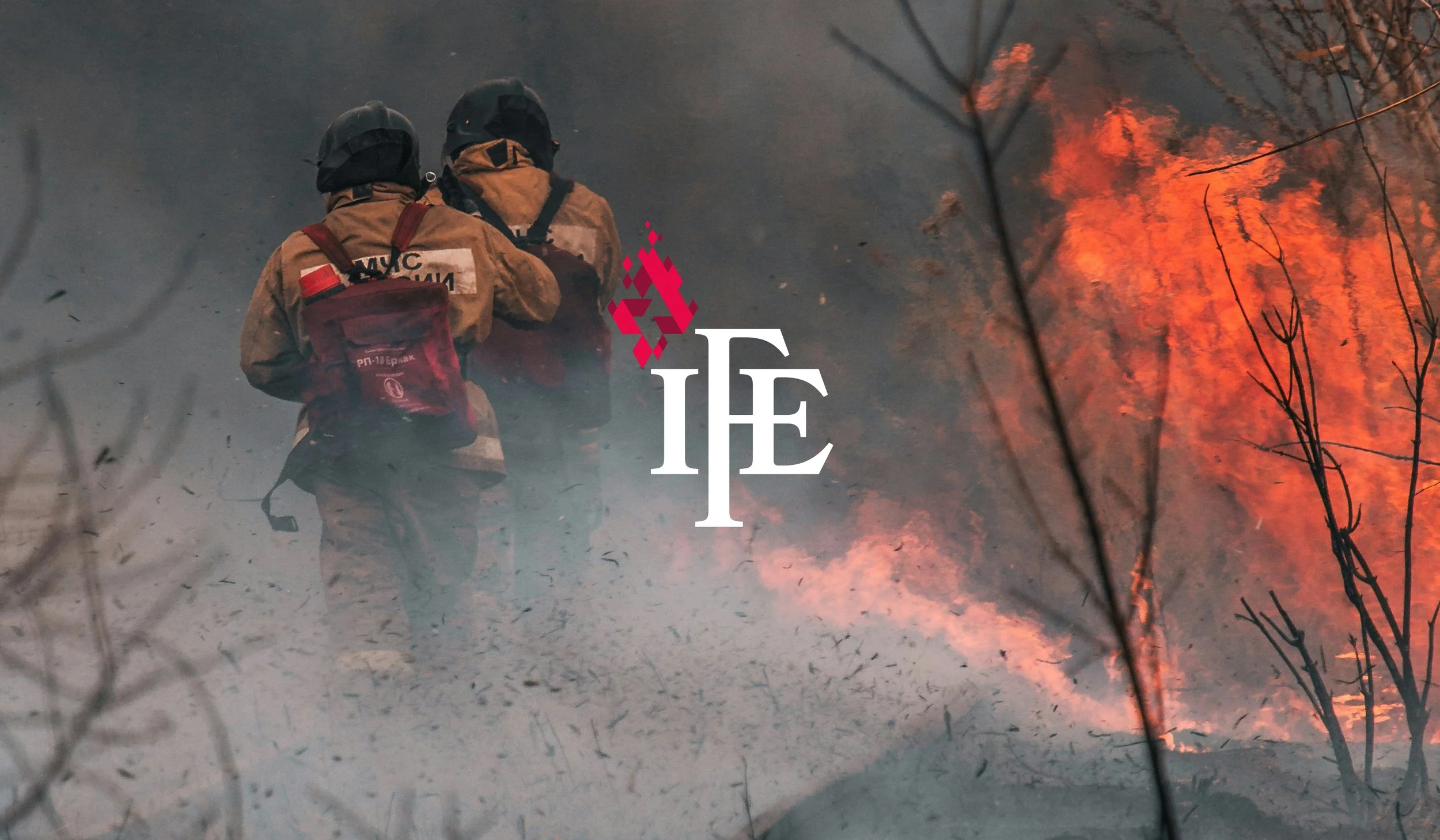 Two firefighters in protective gear facing a large wildfire, with flames and smoke in the background.