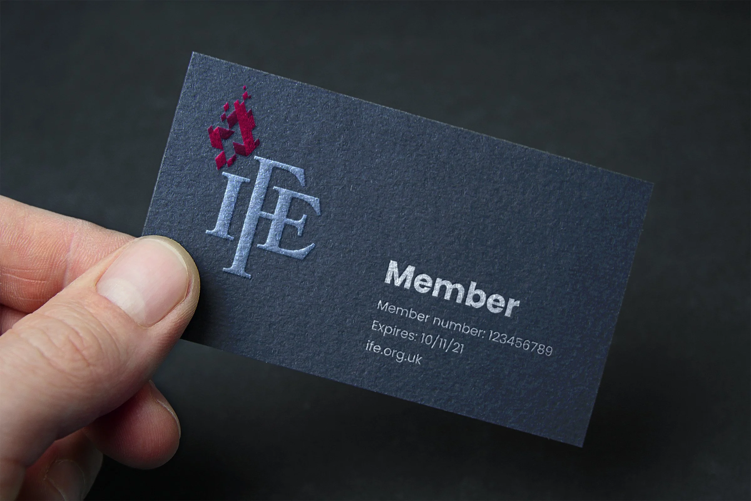 Close-up of a person's hand holding a black membership card with a red and silver logo and white text.