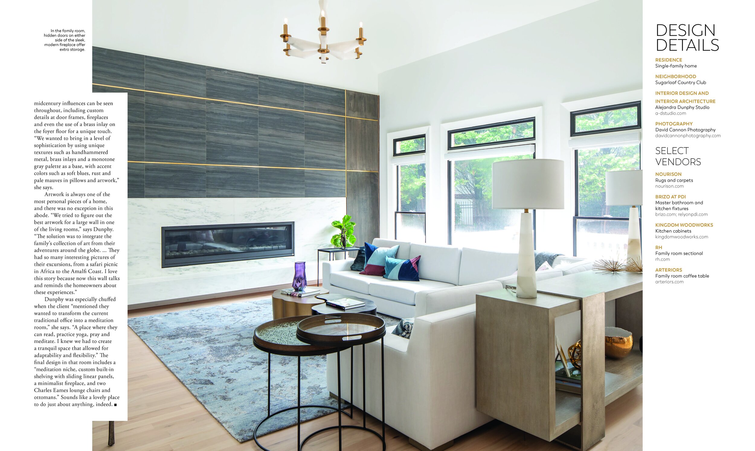 Modern living room with a white sectional sofa and colorful pillows facing a sleek, built-in fireplace. The room features large windows, a patterned rug, two round accent tables, and a contemporary lamp on a stylish console table. Decor includes a pu