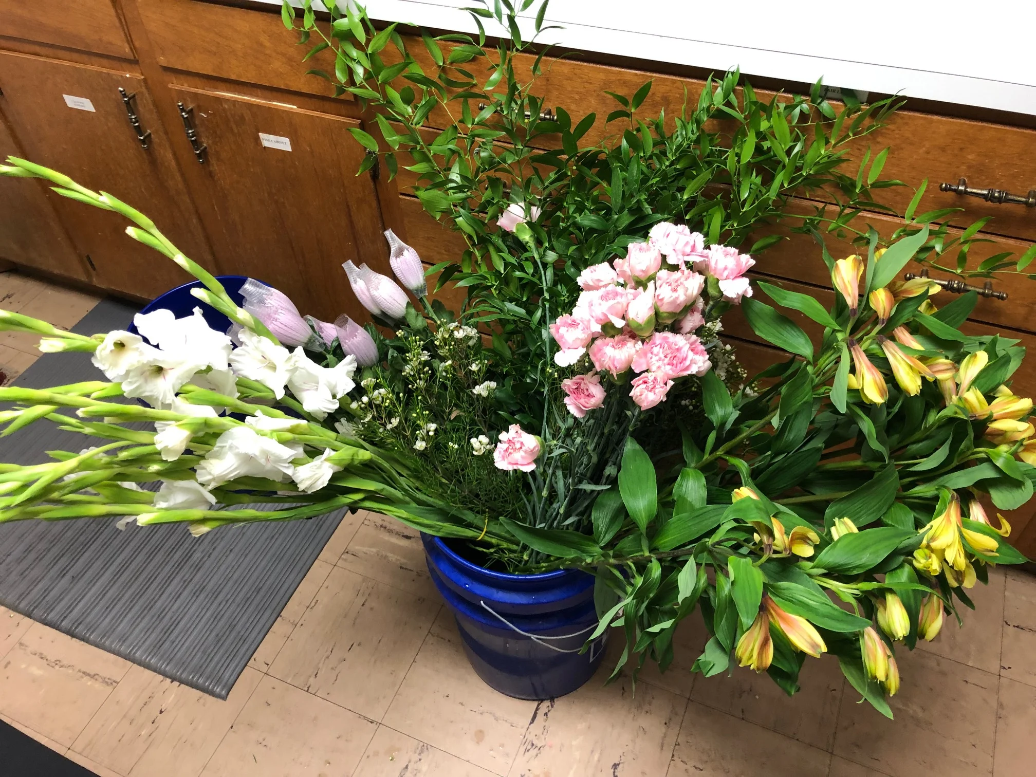 Pink carnations, yellow alstroemeria, lavender Fuji mums, white gladiolas, white wax flower and Italian ruscus.