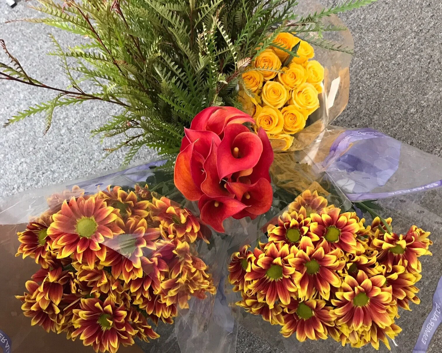 Yellow roses, yellow/rust button daisies, rust mini calla lilies, and grevilla