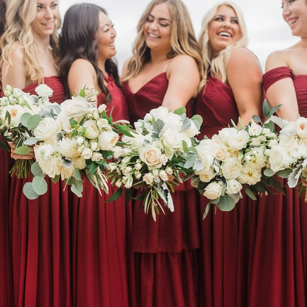 Crimson-clad and joyfully in step&mdash;
A sisterhood of style carrying bouquets that whisper elegance in ivory and sand. Proof that timeless blooms and bold gowns make magic under overcast skies.
.
.
.
#bridesmaidsquad #weddingflowers #bridalpartygo