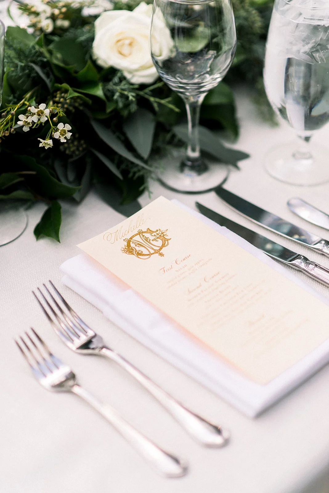 Wedding menu and gold monogram at a white-and-green Sonnenalp place setting.