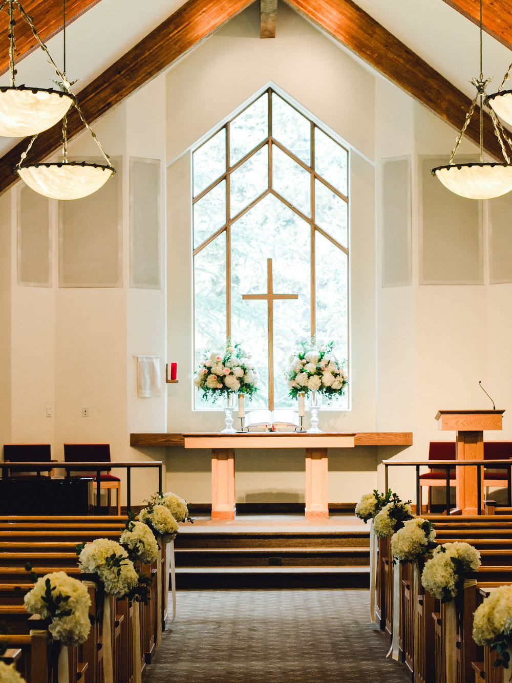 Wedding ceremony flower arrangements on pews and altar with roses and hydrangea at Vail Interfaith Chapel