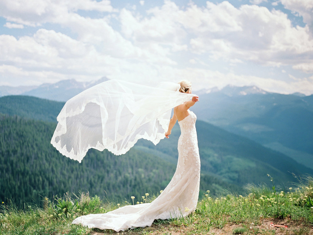 A bride with her veil in a gust of wind on a mountain top in Vail